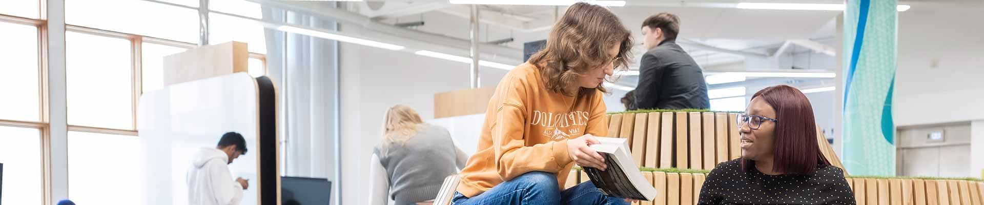 2 female students sitting in Student hub looking at books