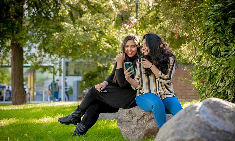 Two female students sat outside looking at a mobile phone