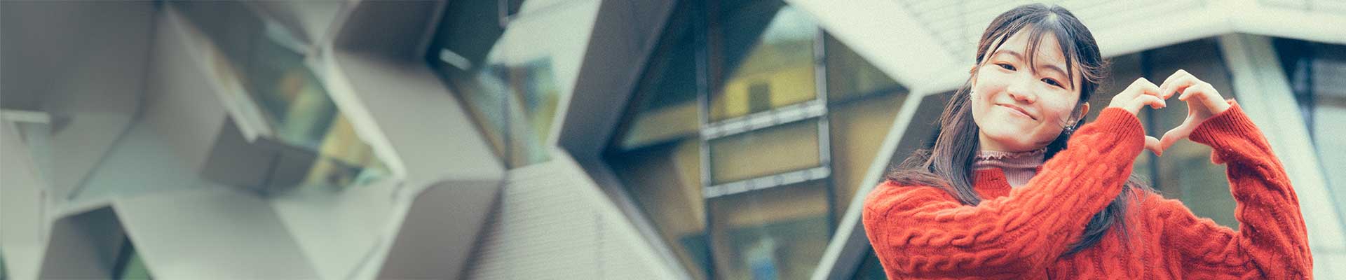 female student standing in front of the EEC building making heart shape with her hands