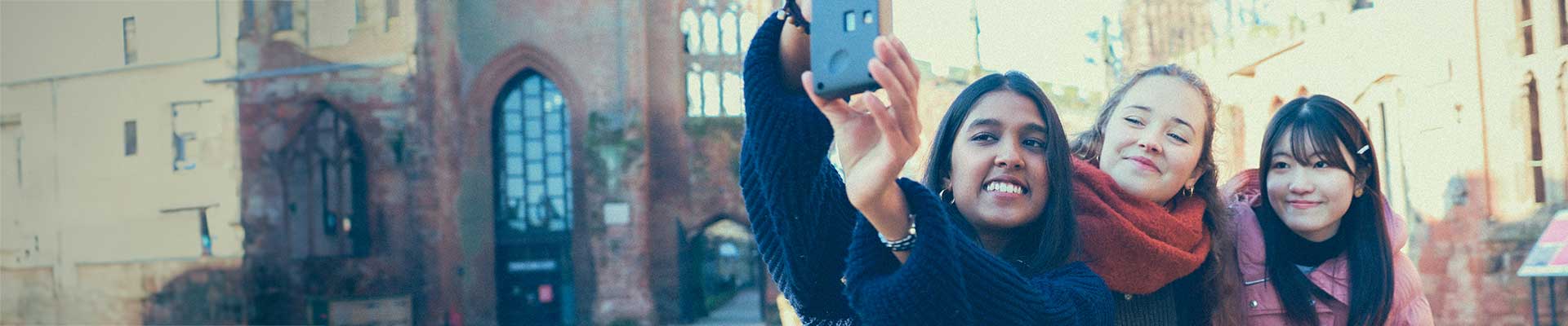 Three students sitting in the Cathedral ruins taking a selfie