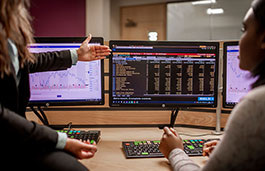 Student and lecturer looking at financial figures on computer monitors..