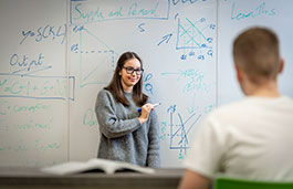 Female in glasses stood in front of white board talking to class.