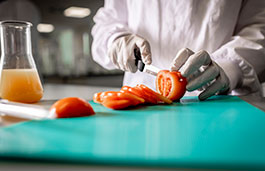 Hands in gloves cutting a tomato.