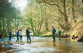Group of geography students using measuring equipment in a river.