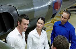 three students looking at a lecturer standing in front of an aeroplane