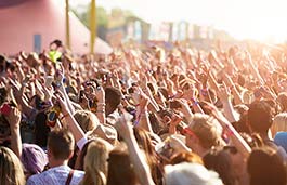 Large crowd at a concert with arms up facing the stage on a bright sunny evening