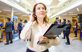 Someone dressed smart stood in a Coventry University environment holding a clipboard and communicating over a pair of headphones