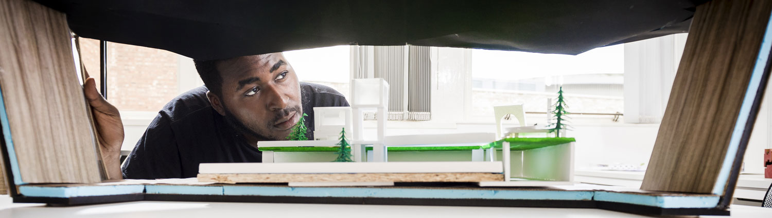 Student in a library surrounded by books looking at a diorama 