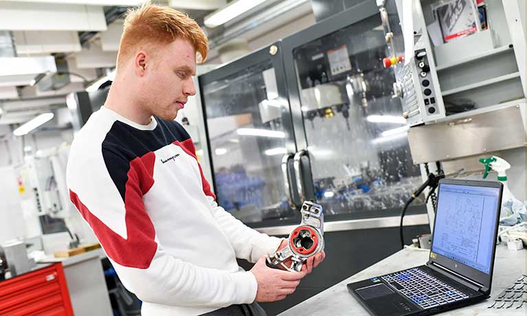 Ali Haddow Motorsport Engineering working on a component with a laptop on the desk in front of him