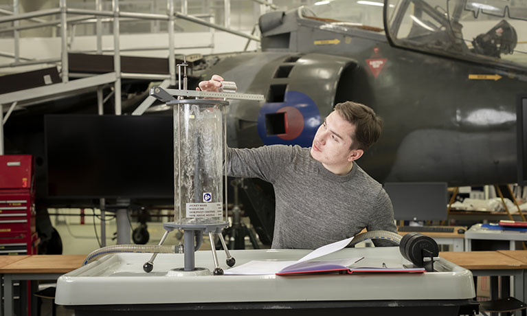 Male student in front of a jet plane using a measurement tool