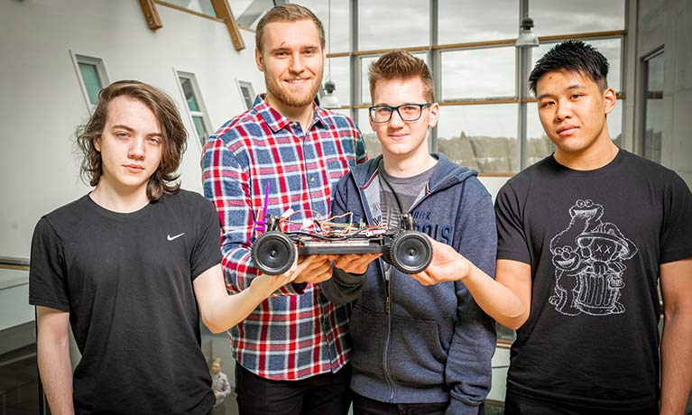 four male computer science students standing in a row showing a model car