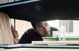 Student in a library surrounded by books looking at a diorama 