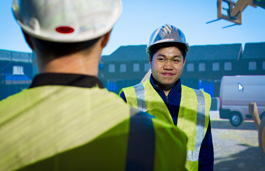 Two people at work talking to each other wearing fluorescent jackets and helmets