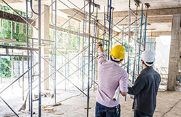 Two males wearing hard hats pointing at scaffolding