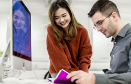 Man reading from a purple booklet and a lady looking at him reading