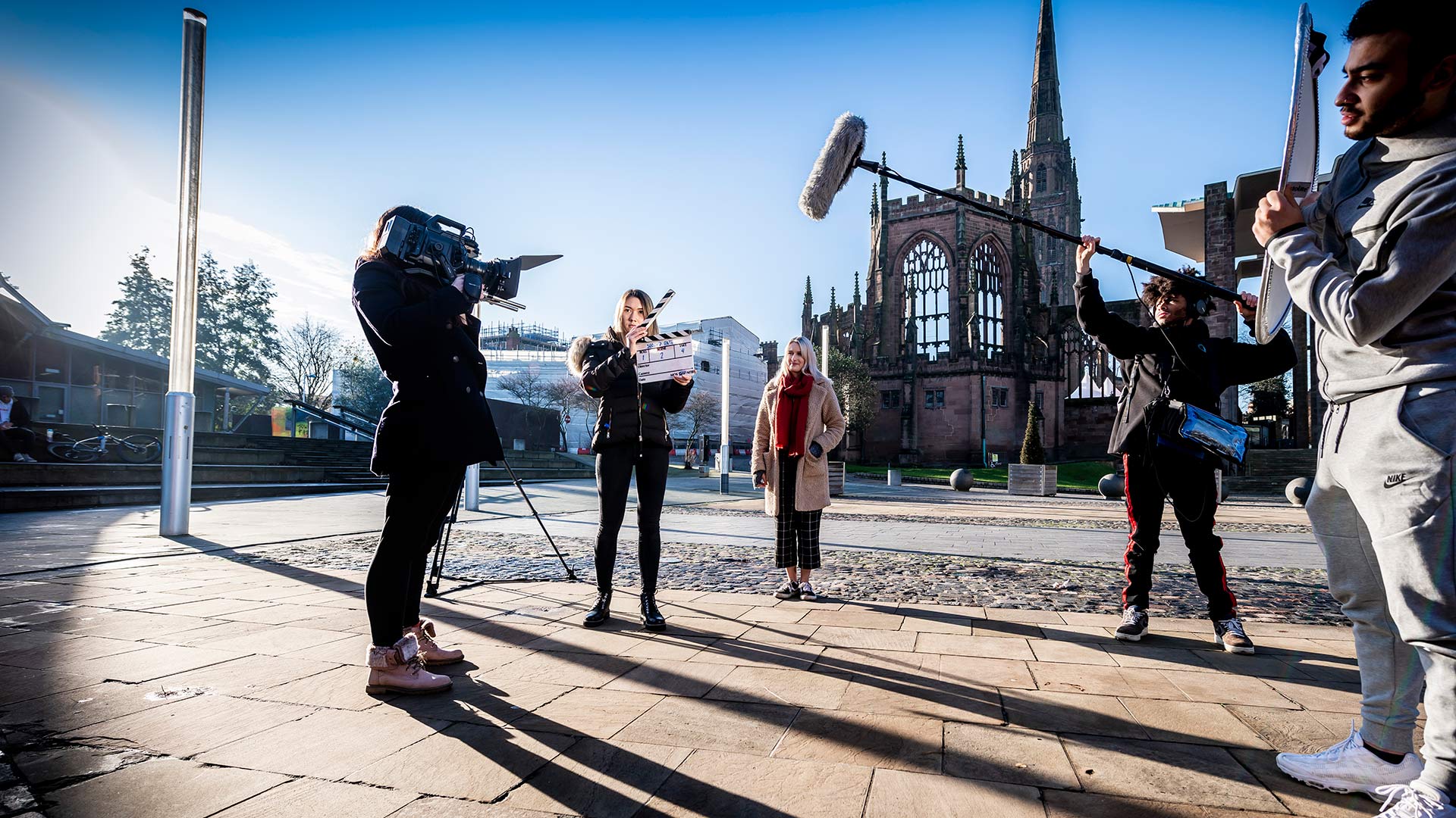 Media Production student with a clapperboard and two students in the background with filming equipment