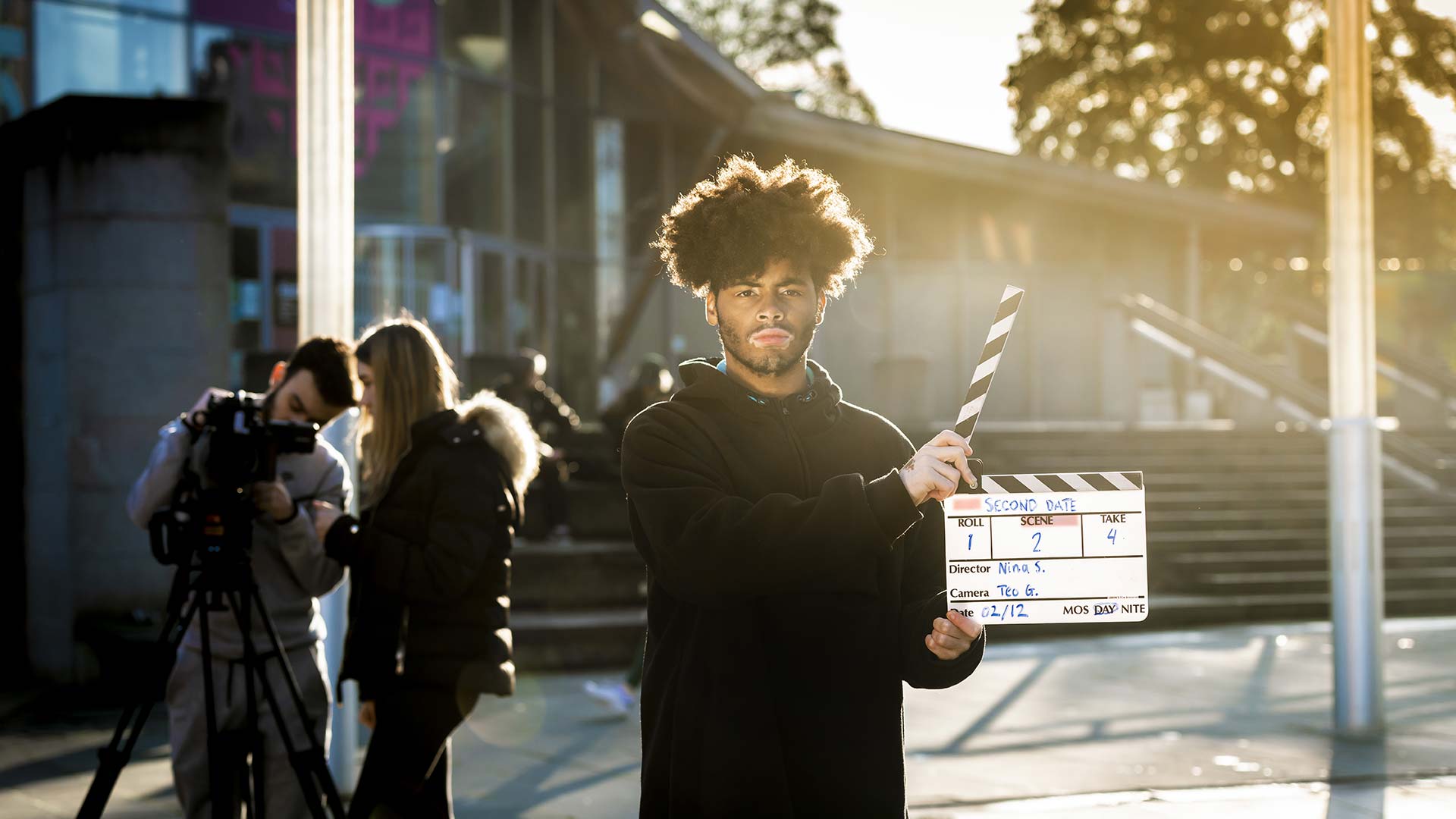 Media student working with a group on an outside shoot, and holding up a clapperboard.