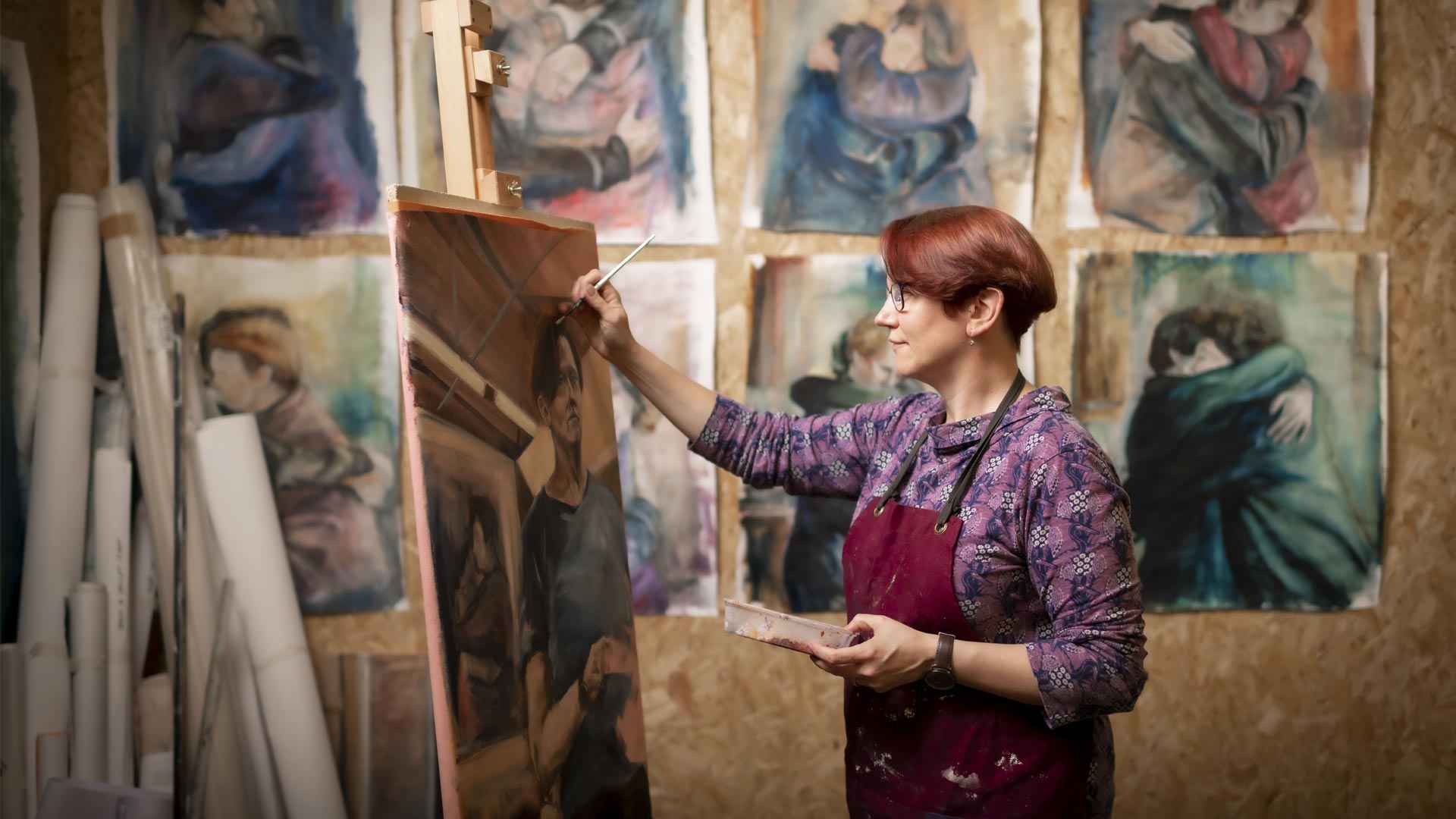 Student painting on a canvas with multiple canvasses on the wall behind them