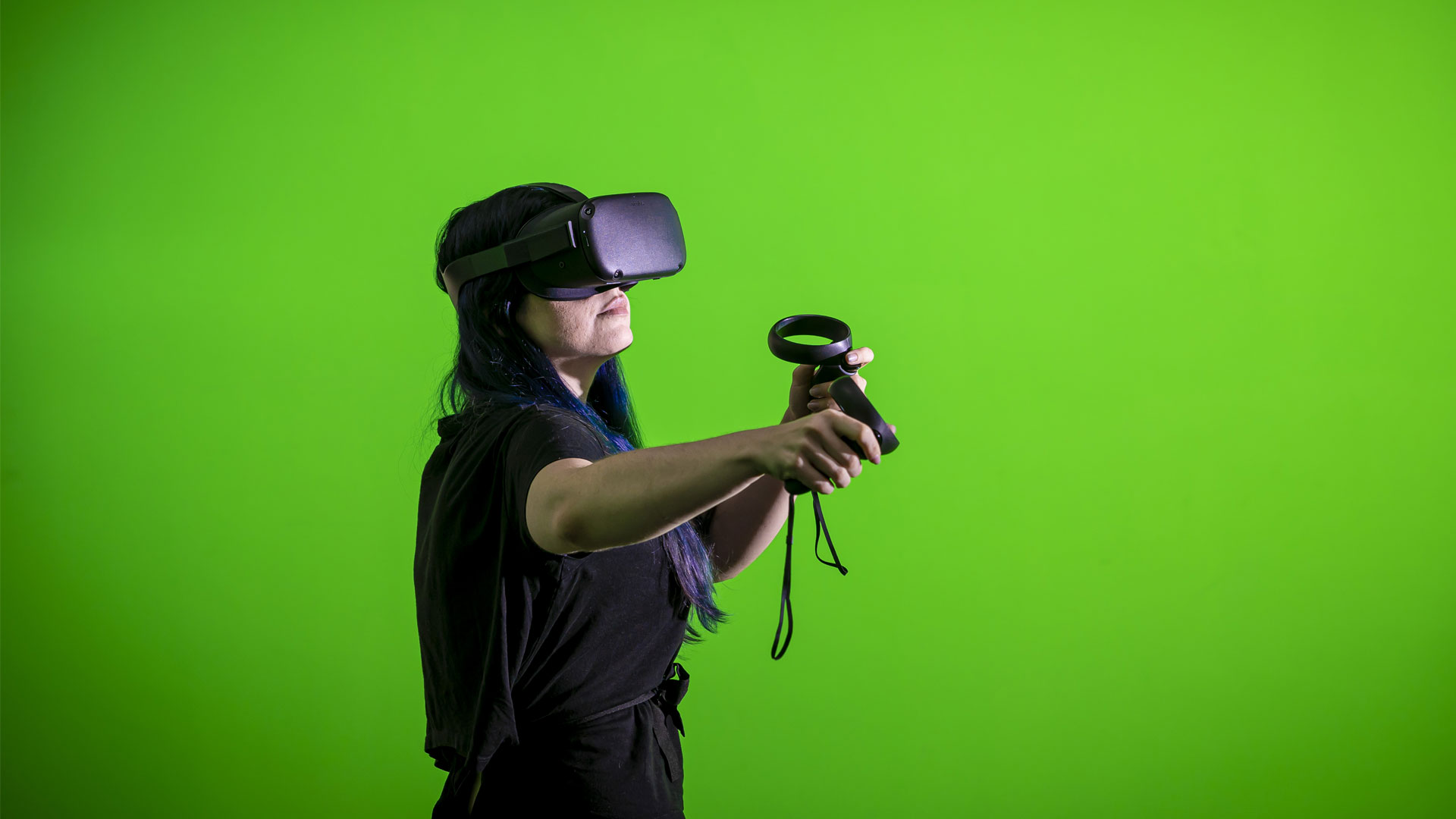 Student using a VR headset in front of a green screen in the Tank Studio.