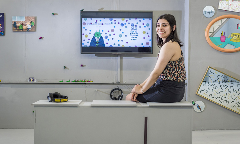 Student in the studio surrounded by drawings and a large flat screen