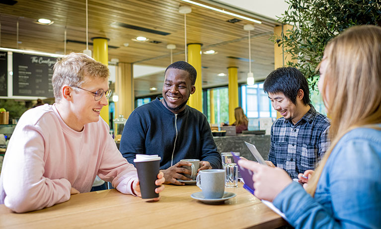 Group of 4 students chatting at a table in a coffee shop.