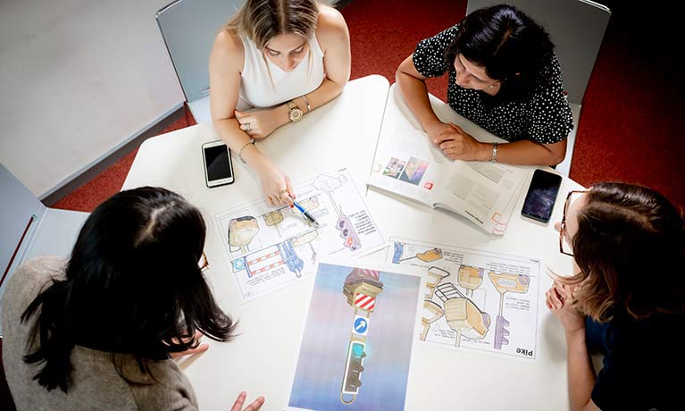 students looking at designs around a table