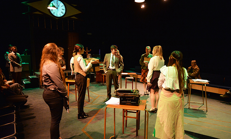 Students in a dark lit performance theatre acting with chairs as props