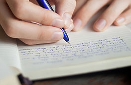 Close up of a hand holding a blue pen writing in a notebook