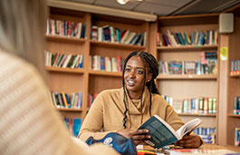 A girl in a library, smiling into the distance whilst holding a book