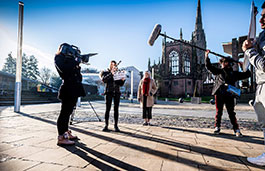Media Production student with a clapperboard and two students in the background with filming equipment