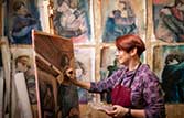 Fine art student painting at an easel with completed works behind her on the wall.