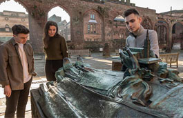 Three students in Coventry Cathedral grounds looking over a sculpture of a man laying down