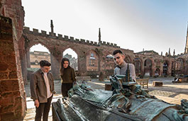 Three students studying a monument in the Coventry Cathedral ruins