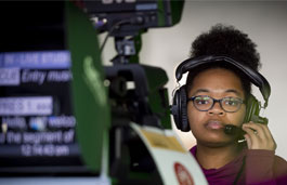 Student with a headset on in front of an autocue in the Media TV Tank