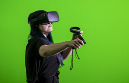 Student using a VR headset in front of a green screen in the Tank Studio