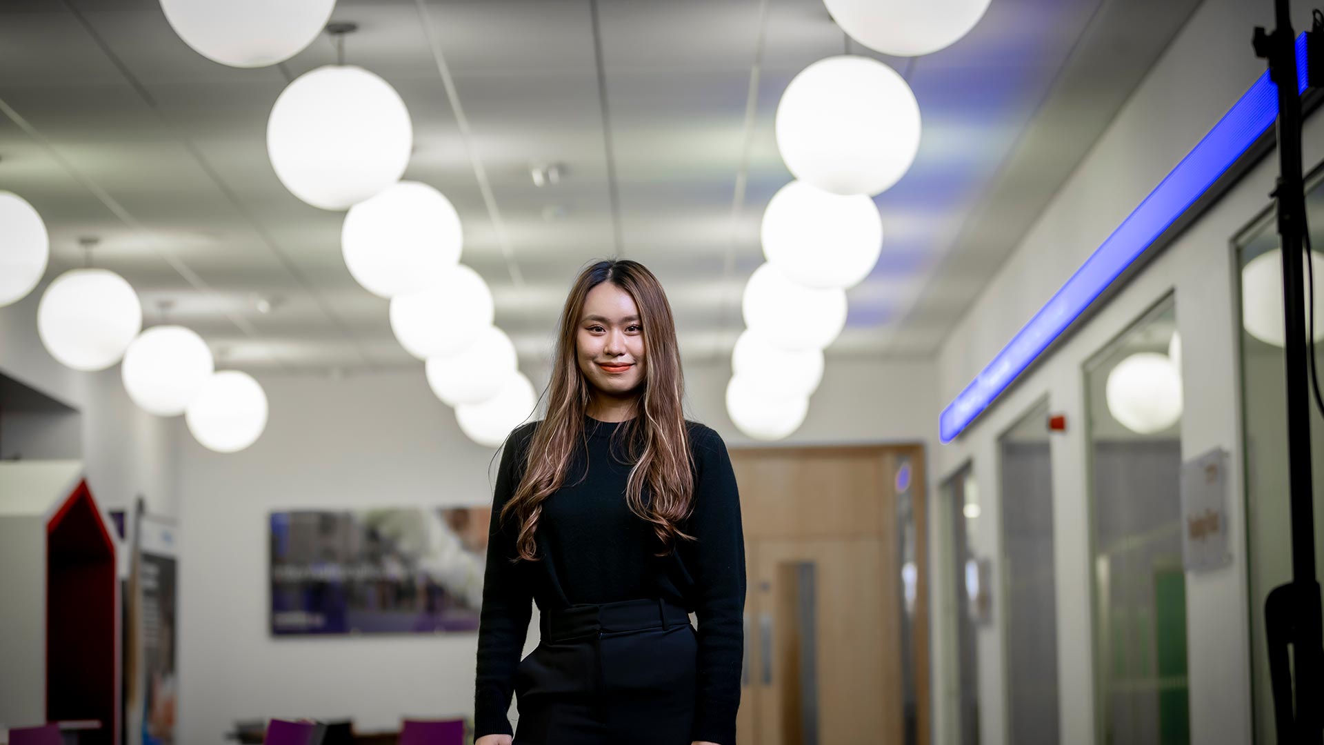 Student stood inside the william morris building smiling with circular lights in the background