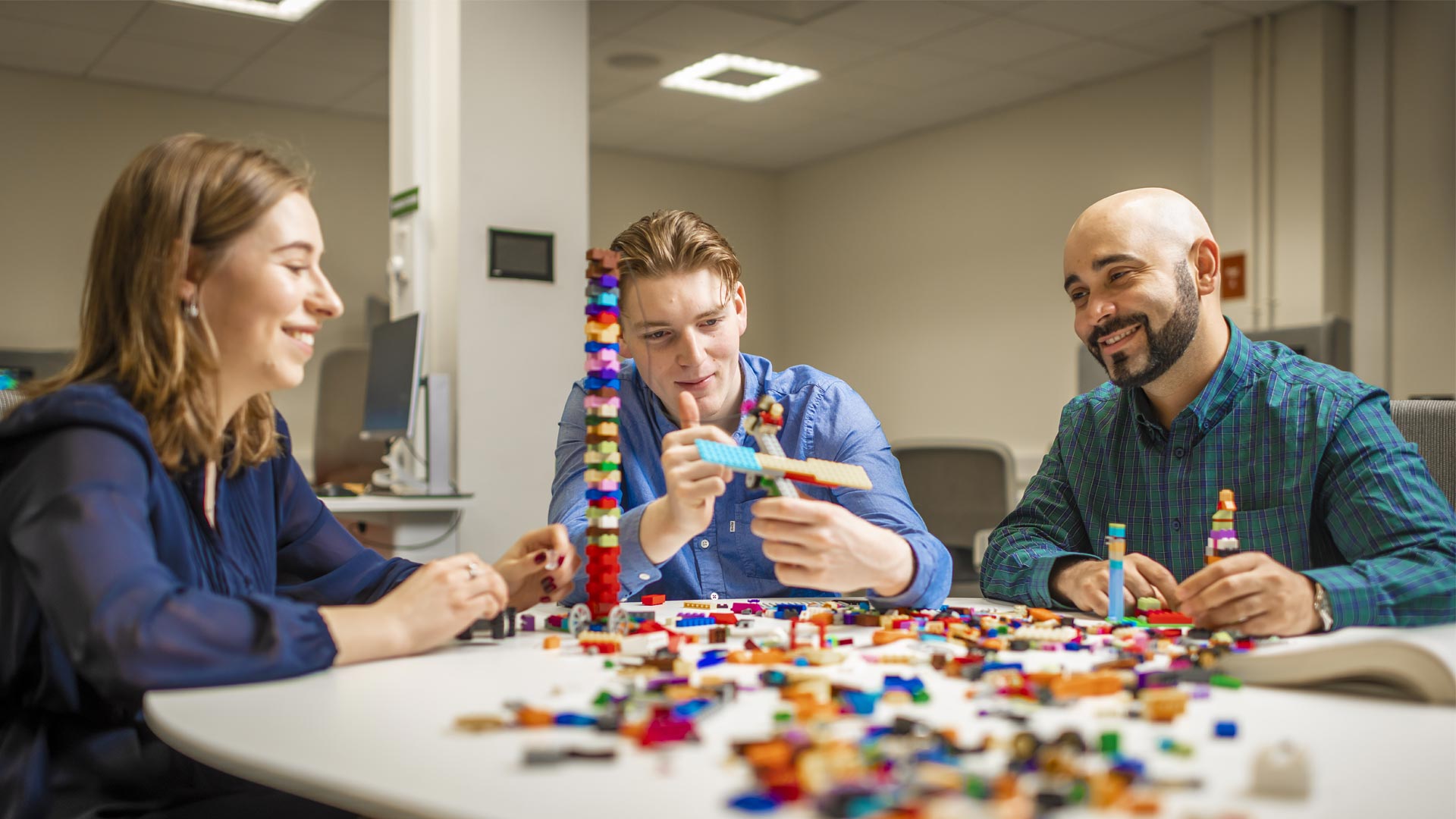 Three students around a table in a classroom working with building blocks 