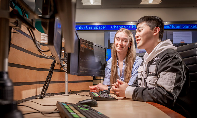 Two students smiling, looking at a bank of screens