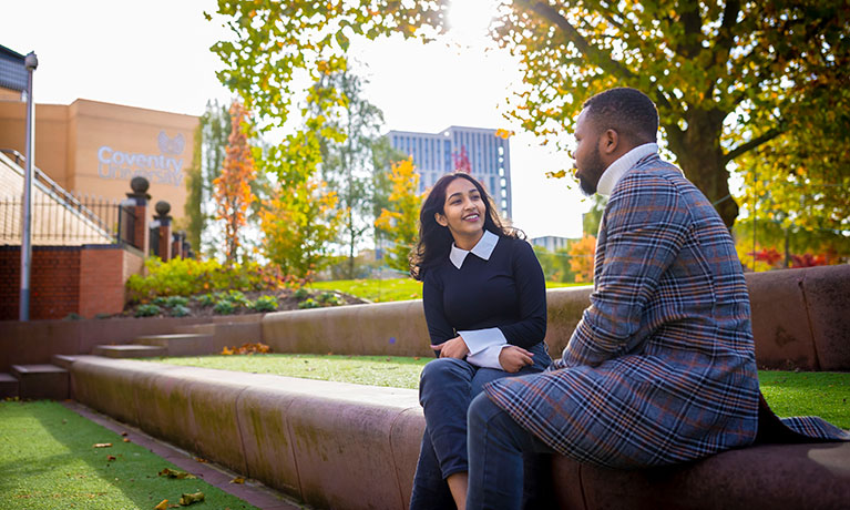 Two students sitting talking in a garden, with one turned away from the camera