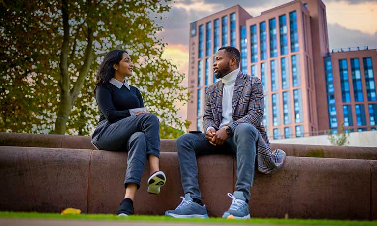 two students chatting on a wall outside the university campus