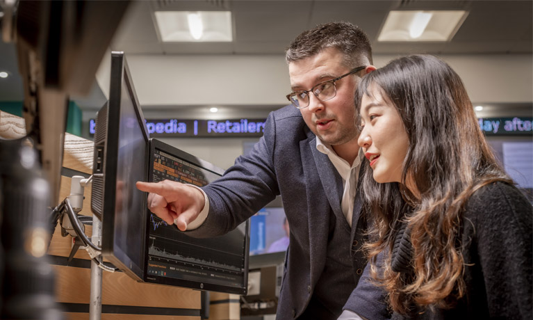 Lecturer showing a student something on a Bloomberg terminal in the trading floor