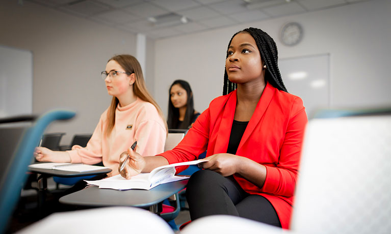 Three students in a classroom taking notes