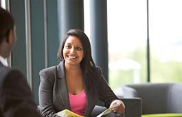 Young professional woman chatting to a man sitting at a table 