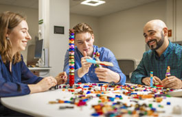 Three students around a table in a classroom working with building blocks