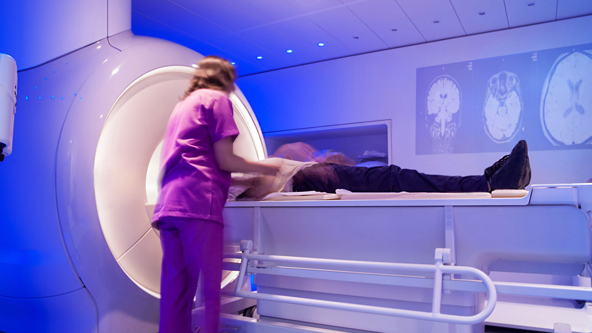 female in scrubs preparing a patient who is lying down in a CT scanning machine