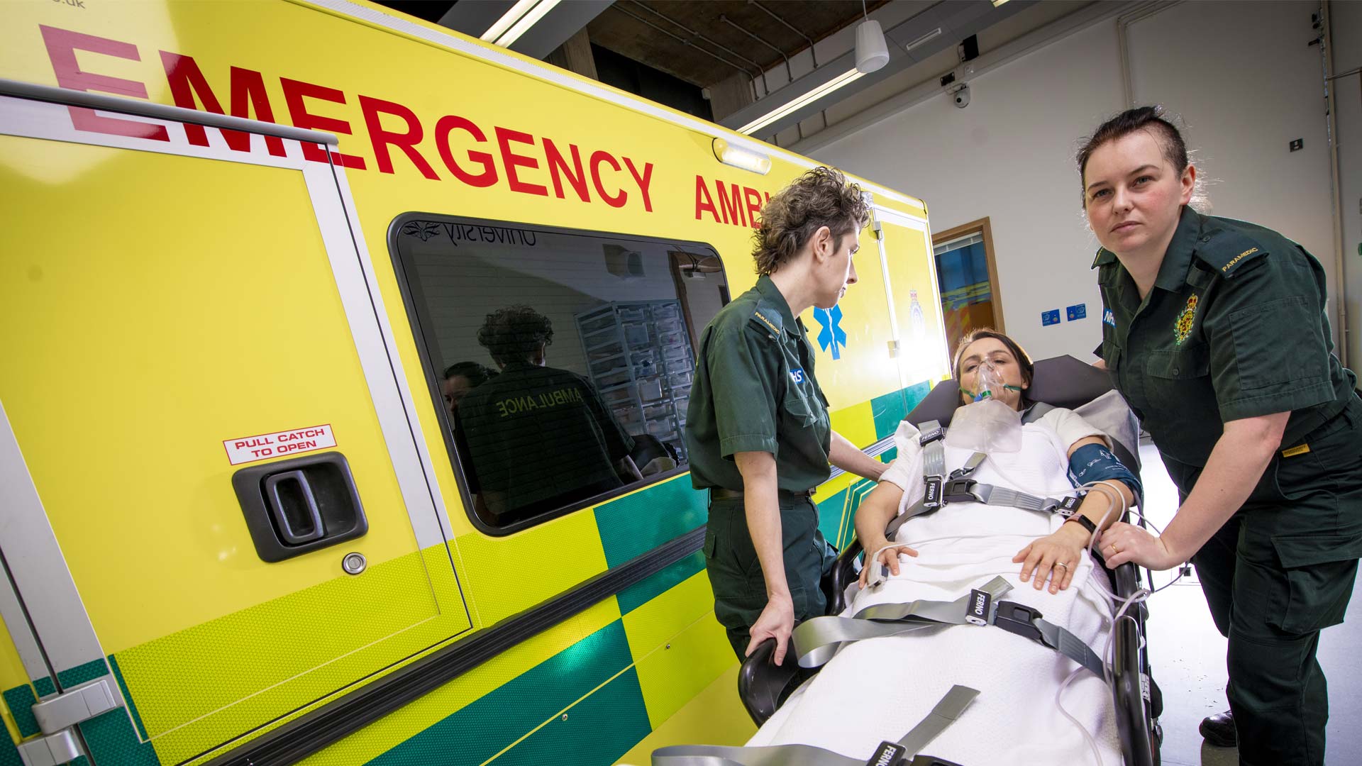 Two paramedic students with a patient on a trolley outside an ambulance