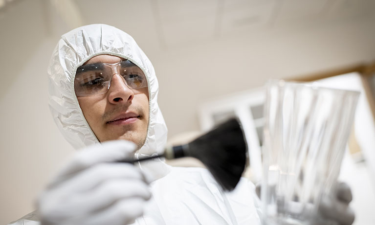 Man in paper suit with glasses dusts a glass for prints using a big brush