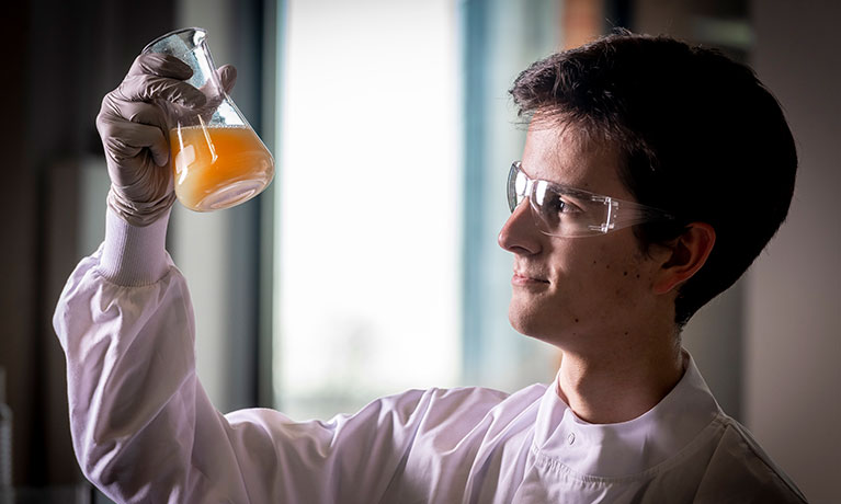 Young male looking at a petri dish containing some orange fluid 