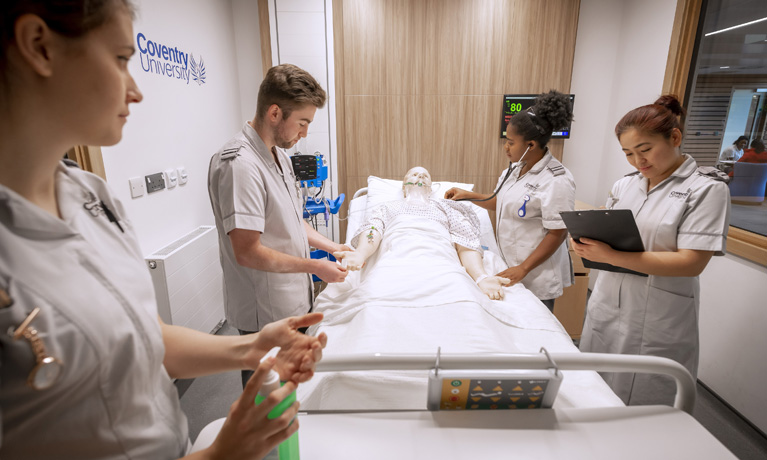 Group of nursing students practicing in a mock examination room with a training mannequin