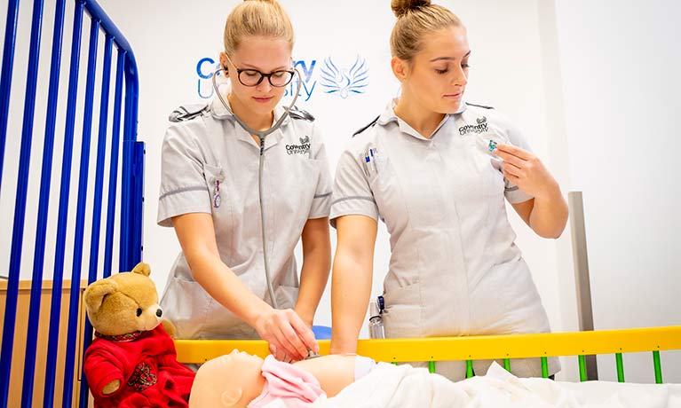 Two nurses doing observations on a baby in a cot